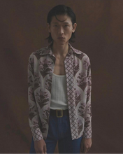 Load image into Gallery viewer, Person wearing a patterned shirt over a white top with blue pants against a dark background