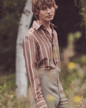 Load image into Gallery viewer, Man wearing a striped shirt and beige pants standing in a natural setting with trees and flowers.
